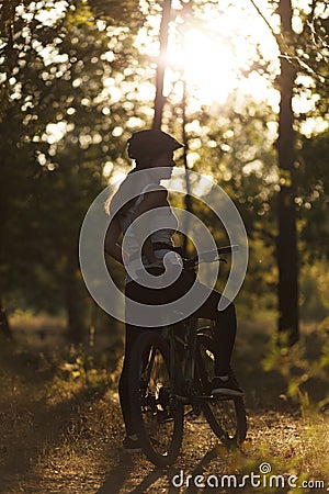 Silhouette of a woman biker in the forest in the rays of the sunset. Training in nature, escape from the city Stock Photo