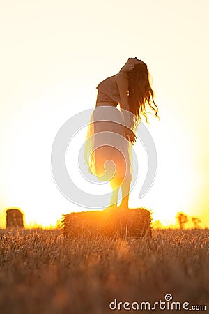 Silhouette woman figure at sunset standing on hay stack, beautiful romantic girl posing outdoors in field, freedom concept Stock Photo
