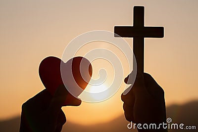 Silhouette of woman hands praying with cross and holding a red heart ball in nature sunrise background, Crucifix, Symbol of Stock Photo