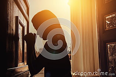 Silhouette of woman kneeling and praying in modern church at sun Stock Photo