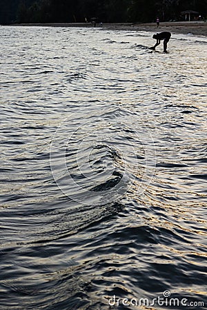 Silhouette woman over the sea wave surface that reflected with blue, yellow sky color in the evening in Koh Mak Island. Editorial Stock Photo