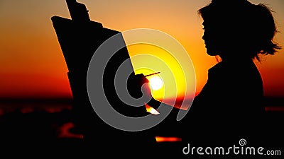 Silhouette of a woman painting a picture with paint brush and palette on canvas on an easel, girl face profile engaged in art in a Stock Photo