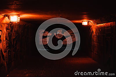 A silhouette of a woman passing in a dark red rusty tunnel with dim orange lights Editorial Stock Photo