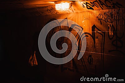 A silhouette of a woman passing in a dark red rusty tunnel with dim orange lights. Her purse is brightly lit Editorial Stock Photo