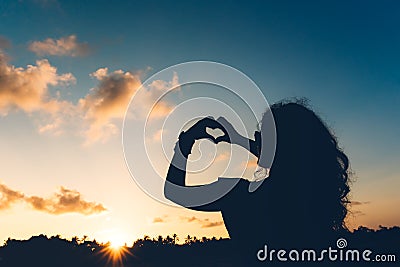 Silhouette of woman showing love, making heart shaped gestures with hands and enjoying sunset at exotic resort Stock Photo