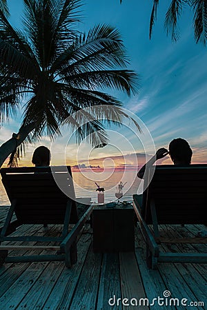 Silhouette woman sit on beach chair having cocktail drink watching sunset over the sea. Stock Photo