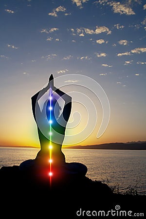 Silhouette of woman sits in a lotus pose on beach sunset view, glowing seven all chakra. Kundalini energy. girl practicing yoga Stock Photo