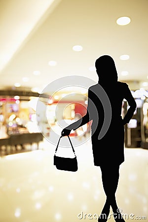 Silhouette of woman standing in a shopping mall ad holding a purse Stock Photo