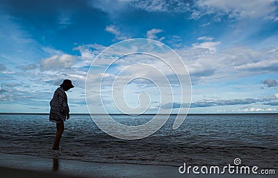 Silhouette woman walking on seabeach in evening with beautiful blue sky over sea water, look lonely and quiet. Stock Photo