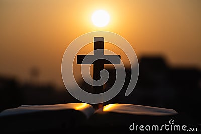 Silhouette of wooden Christian cross on bible with a bright sunrise as background , god Stock Photo