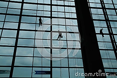 A silhouette of a worker cleaning windows hangs from a rope in the airport building Stock Photo