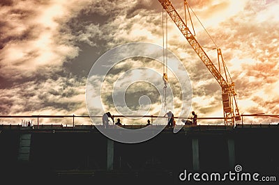 Silhouette of workers on the top of the building construction site with crane and sunset sunlight, image contains film graine. Stock Photo