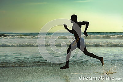 Silhouette of young attractive fit athletic and strong black African American man running at sunset beach training hard and Stock Photo