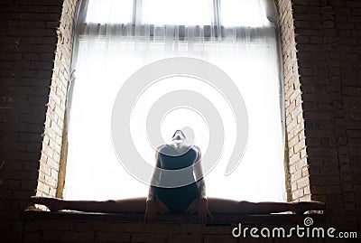 Silhouette of a young, flexible well shaped ballerina sitting on the huge window Stock Photo