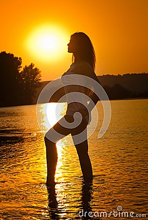 Silhouette of young beautiful woman in the river over sunset sky. Female perfect body contour at beach in twilight scenery Stock Photo