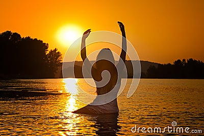 Silhouette of young beautiful woman in the river over sunset sky. Female perfect body contour at beach in twilight scenery Stock Photo