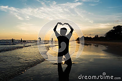 Silhouette of young boy making heart sign with his arms on the b Stock Photo