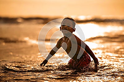 Silhouette of young boy playing crazy happy and free at the beach splashing with water playing with sea waves jumping and having Stock Photo