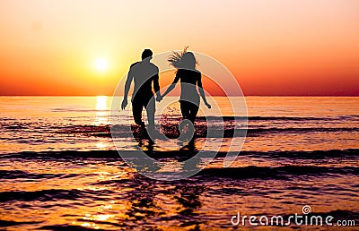 Silhouette of young fitness couple walking inside the water at sunrise - Multi race people having fun on vacation - Romantic and Stock Photo