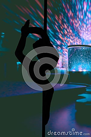 Silhouette of a young flexible girl hanging in a dancing pole performing in a strip club Stock Photo