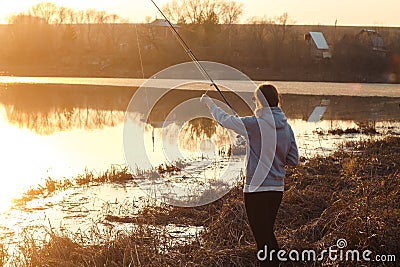 Silhouette of a young girl fishing at sunset near the lake Stock Photo