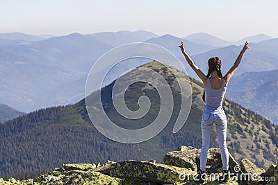 Silhouette of a young happy beautiful slim girl with long braids standing on big rocks in mountains lifting hands, meeting a raisi Stock Photo