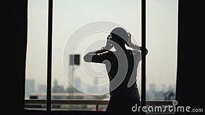Silhouette of young man dancing ad listening music in wireles headphones stand on hotel room balcony Stock Photo