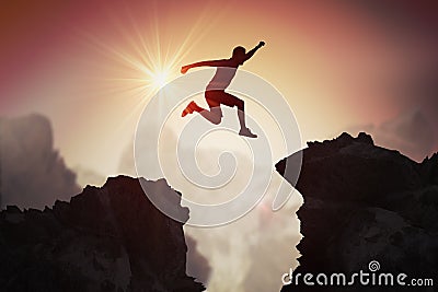 Silhouette of young man jumping over mountains and cliffs at sunset Stock Photo