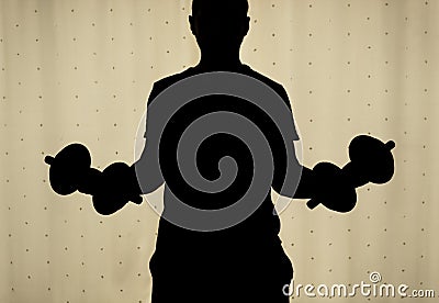 Silhouette of a young man making a biceps dumbbell curl with yellow curtains at background. Stock Photo