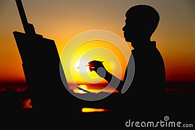Silhouette of a man painting a picture on linen on an easel on nature, painter face profile engaged in art in a field at sunset Stock Photo