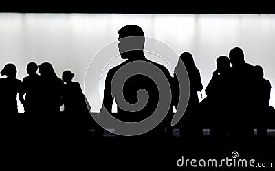 Silhouette of young man standing alone and a crowd of people walking behind him Stock Photo