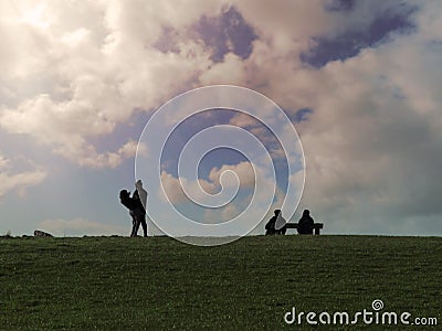 Silhouette of young and old couple against bright cloudy sky. Young pair standing and holding each other in their hands. Older Stock Photo