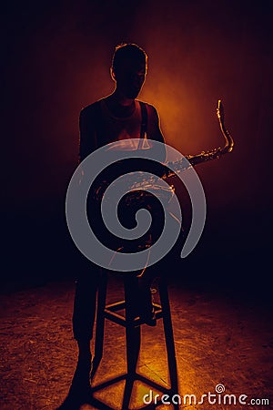 silhouette of young saxophonist sitting on stool Stock Photo