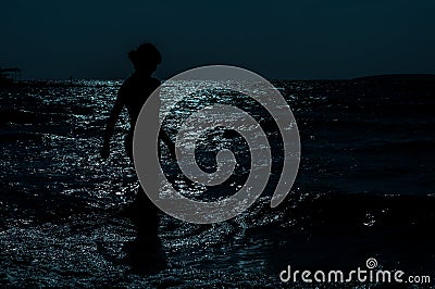 Silhouette of young, slim, woman walking in the sea under the moonlight Stock Photo