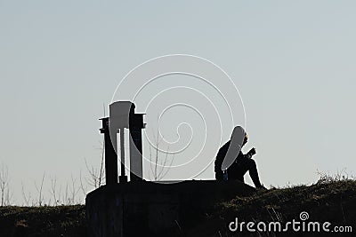 Silhouette of a young standing girl in jogging sportswear near a metal construction. Relax in a romantic atmosphere in nature. The Editorial Stock Photo