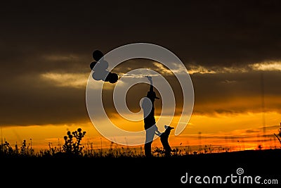 Silhouette of a young woman and her dog at sunset. Outdoors. She is holdings balloons. Love for animals concept Stock Photo