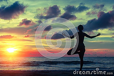 Silhouette young woman practicing yoga on the beach at sunset. Stock Photo