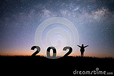 Silhouette of young woman raising hands prepare to welcome the new year 2022 and looking view night sky, star and milky way alone Stock Photo