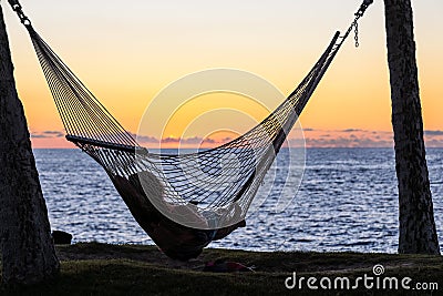 Silhouette of a young woman resting in a hammock and watching sunset over Pacific ocean Stock Photo