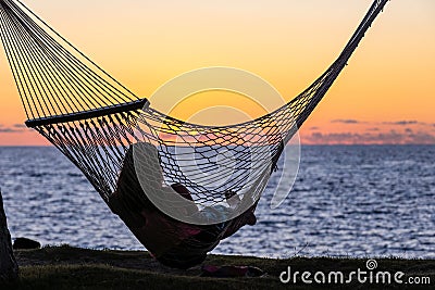 Silhouette of a young woman resting in a hammock and watching sunset over Pacific ocean Stock Photo