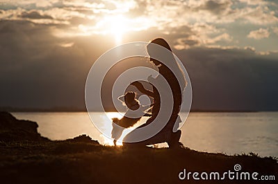Silhouette of young woman training chihuahua small dog on beautiful sea sunset background Stock Photo