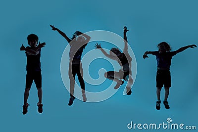 Silhouetted full length shot of four little sportive kids looking joyful while posing, jumping isolated over blue Stock Photo