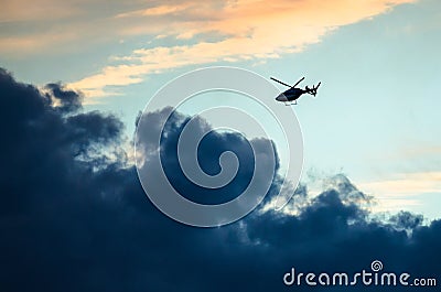 Silhouetted Helicopter Flying Across a Sunset Sky Stock Photo