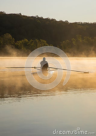 Silhouetted Man Rowing Single Scull on Foggy Water at Sunrise Stock Photo