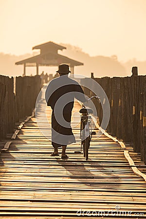 Silhouetted man walks bike along wooden footbridge Editorial Stock Photo