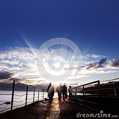 Silhouetted people walking on street over sunset sky Stock Photo