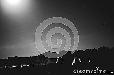 Silhouetted, unrecognizable people camping under full moon Stock Photo