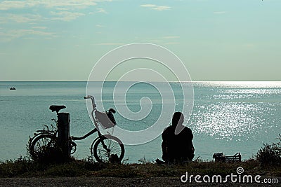 Silhouettes of bicycle and man sitting at the seashore and looking at sea Stock Photo