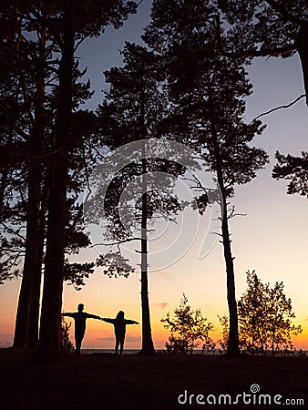 Silhouettes of brother and sister on the pine coast in evening time Stock Photo