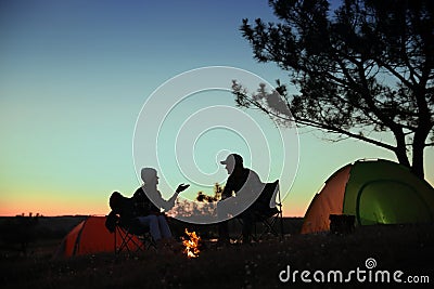 Silhouettes of couple near bonfire in evening. Camping season Stock Photo